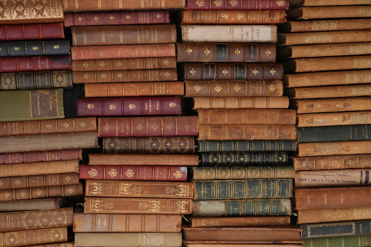 Collection of antique leather-bound books with gold lettering on dark wooden shelf