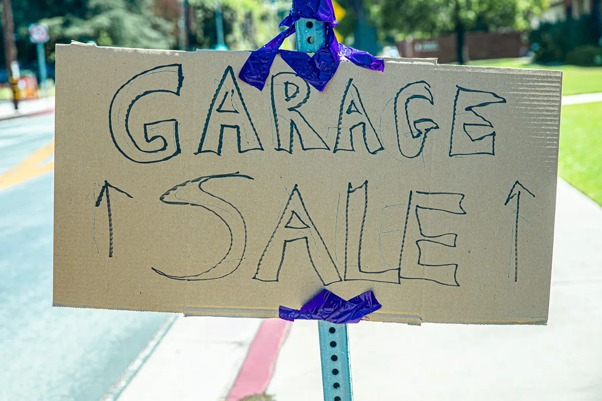 Neighborhood street with multiple garage sale signs and families browsing items