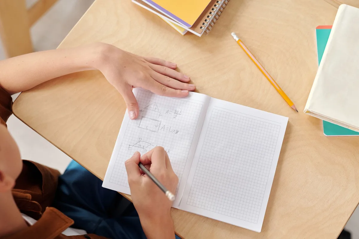 A young student writing math equations in a notebook at a school desk
